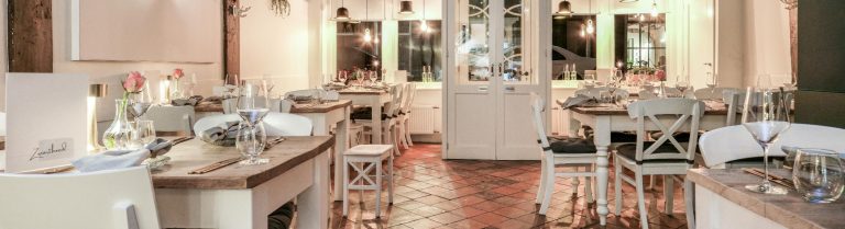 Gezellig restaurantinterieur met gedekte houten tafels, witte stoelen en een tegelvloer, klaar voor gasten.