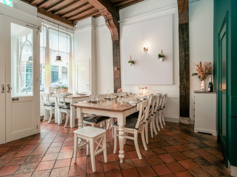 Sfeervol restaurantinterieur met houten tafels, witte stoelen, terracotta tegelvloer en TREKKEN op de glazen deur.