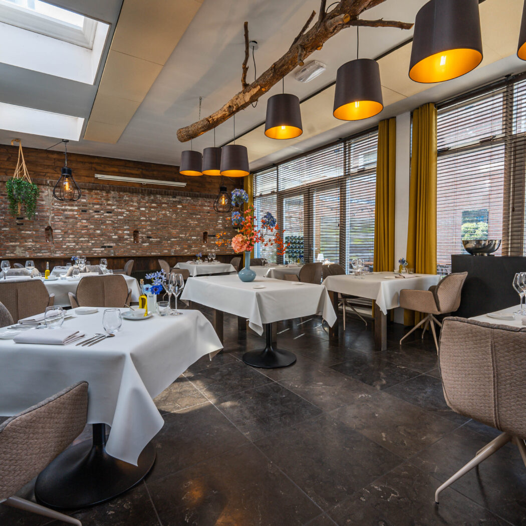 Modern restaurantinterieur met opgedekte tafels, moderne stoelen, bakstenen muur en lampen aan een houten tak.