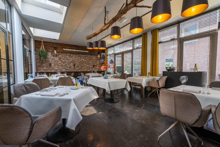 Modern restaurantinterieur met opgedekte tafels, moderne stoelen, bakstenen muur en lampen aan een houten tak.