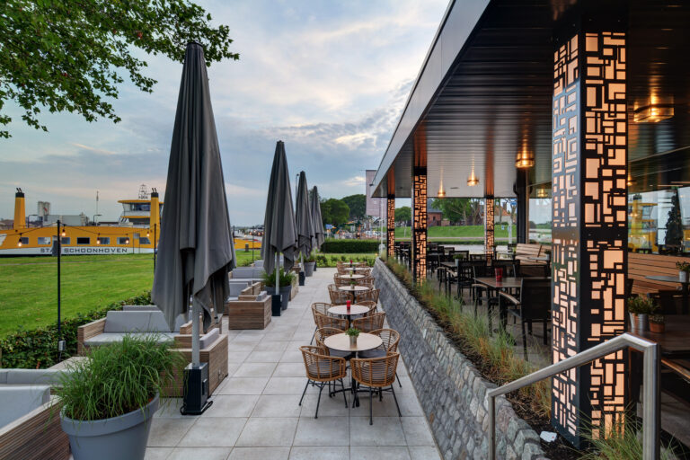 Ruim buitenterras met loungebanken, caféstoelen en decoratieve pilaren, aan de waterkant met veerboot Stad Schoonhoven.