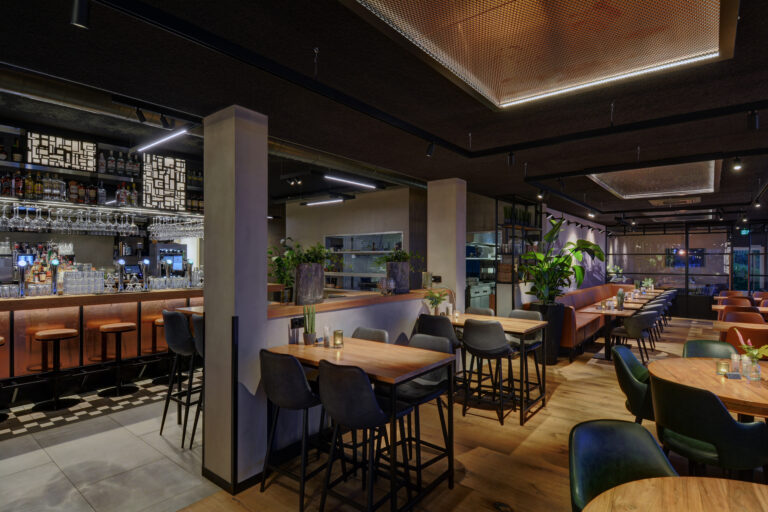 Een modern en stijlvol restaurantinterieur met een goed gevulde bar, diverse zitplekken en warme verlichting.