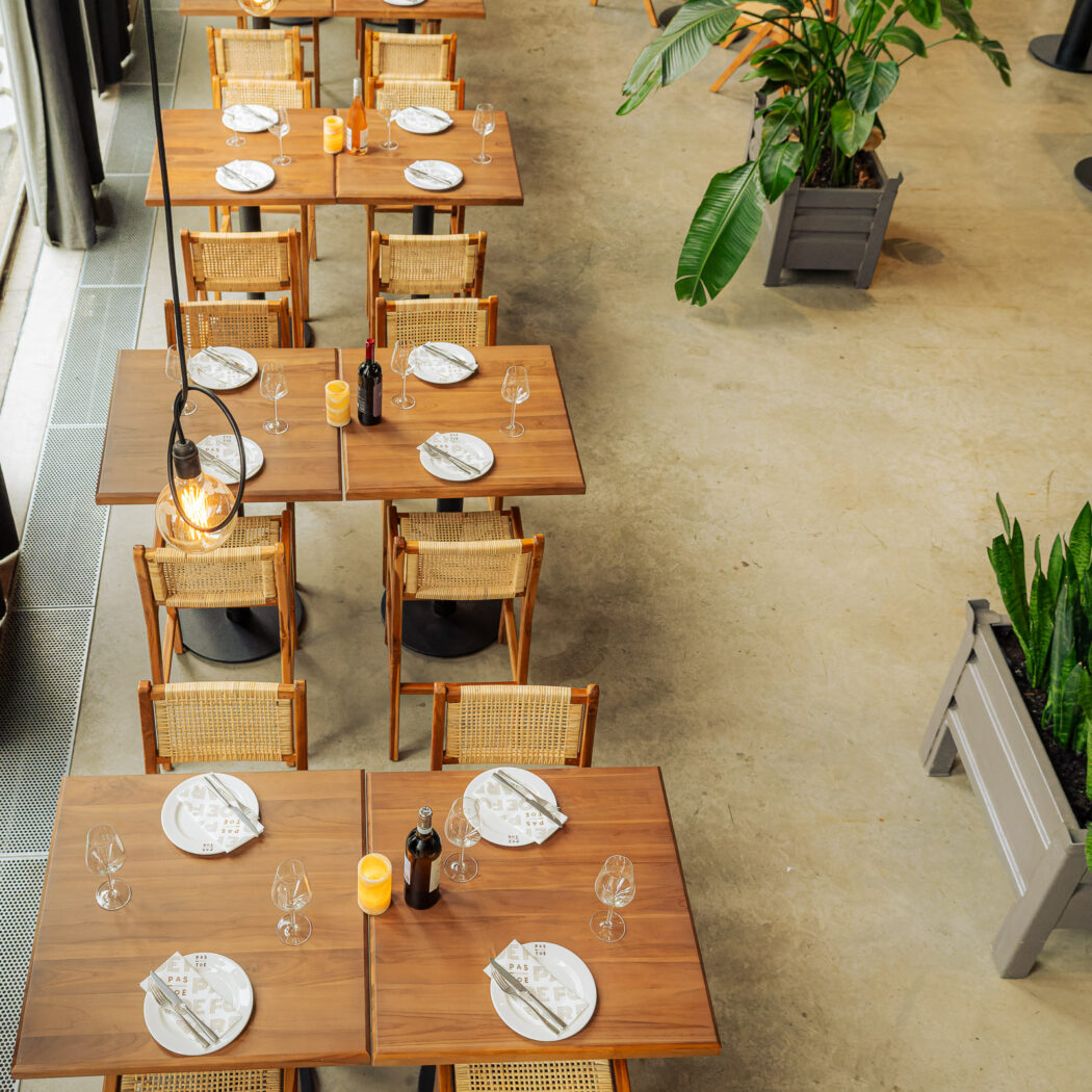 Modern restaurant interieur met gedekte houten tafels, rieten stoelen, wijn, planten en borden PAS DE PAS.