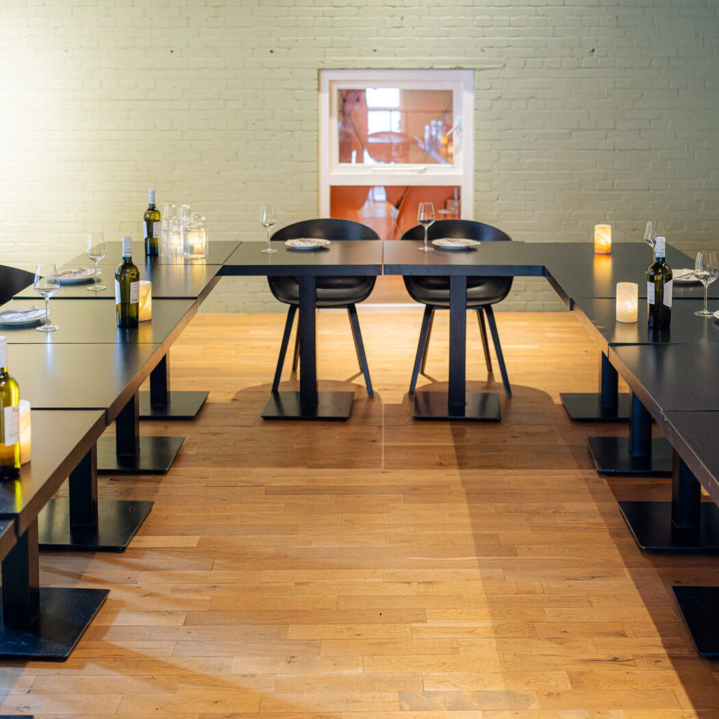 U-vormige zwarte eettafel in een moderne ruimte, gedekt met borden, glazen, wijnflessen en kaarsen.