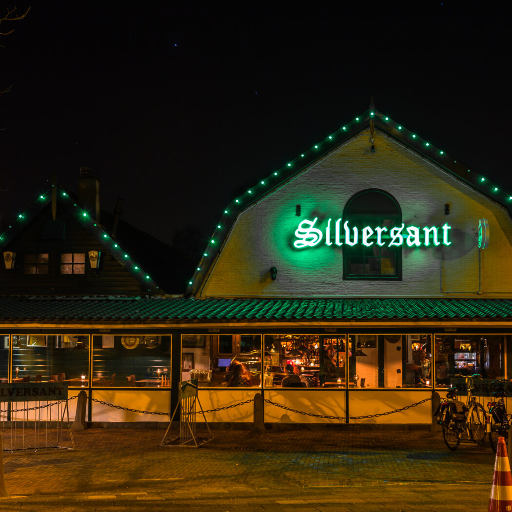 Nachtzicht op café Silversant met opvallende groene neonletters en dakrandverlichting.