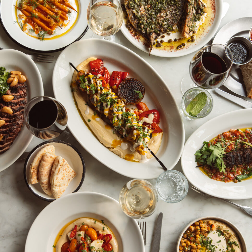 Marmeren tafel vol Midden-Oosterse gerechten: gegrilde vis, kebab, falafel, hummus, geroosterde wortels en wijn.