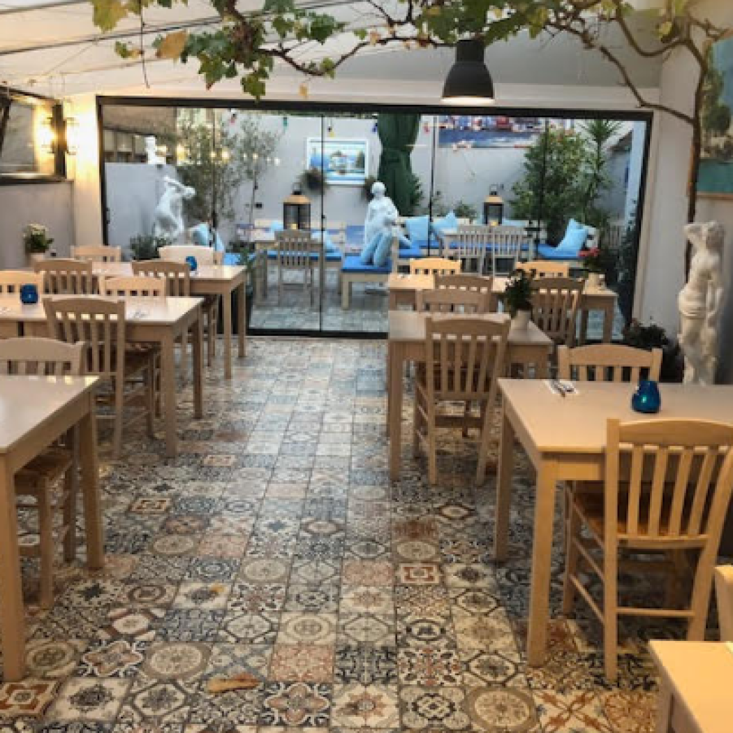 Sfeervol restaurant met lichte houten tafels, patroontegels en uitzicht op een mediterrane patio.