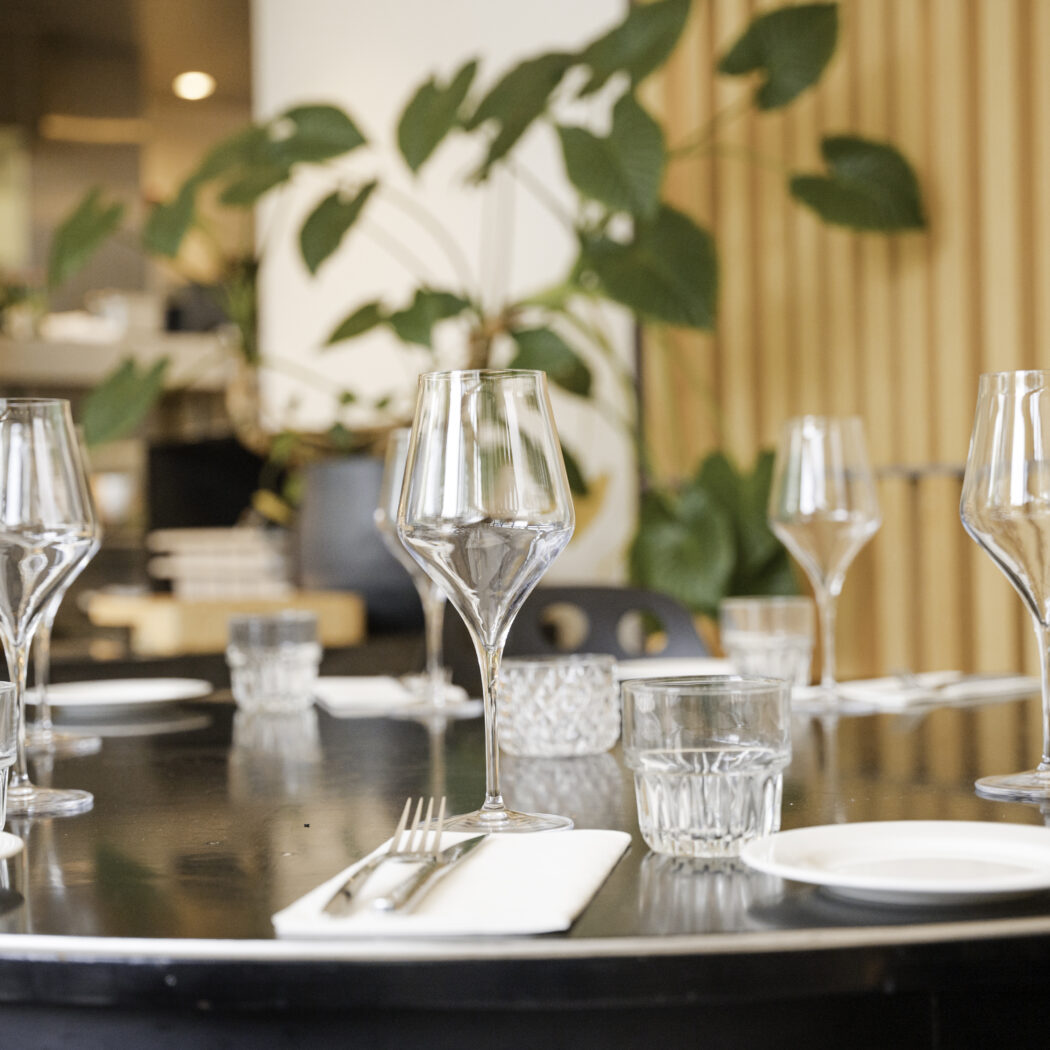 Zwarte ronde tafel stijlvol gedekt met wijnglazen, waterglazen en witte borden in een modern restaurant.