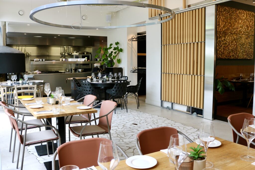 Modern restaurant interieur met ingedekte houten tafels, een open keuken en houten wandpanelen.