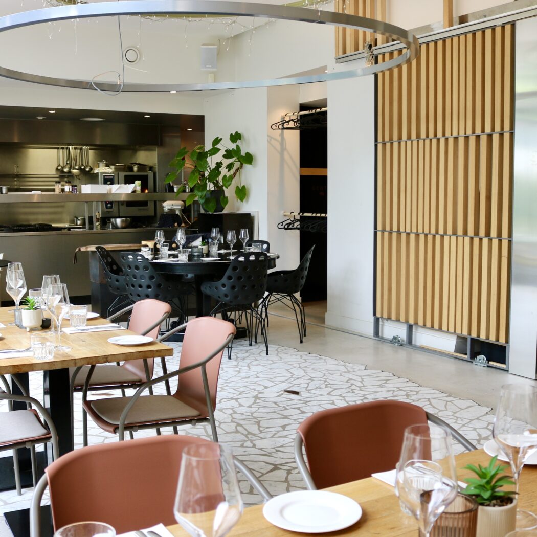 Modern restaurant interieur met ingedekte houten tafels, een open keuken en houten wandpanelen.