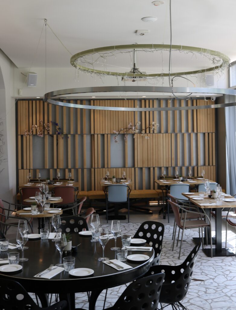 Strak ingericht restaurant interieur met gedekte tafels, houten lambrisering en een opvallende ringlamp.