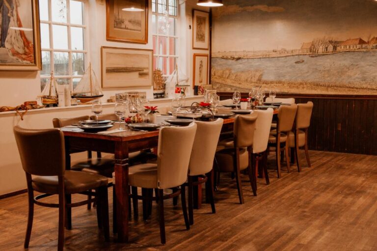 Lange houten eettafel, gedekt voor diner in sfeervol restaurant met maritiem decor en waterlandschap muurschildering.