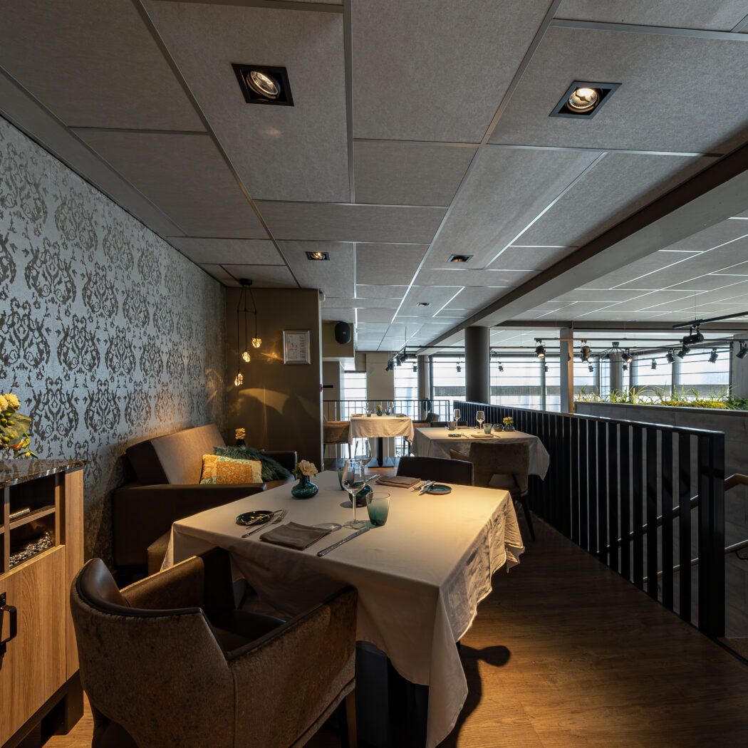 Stijlvol restaurantinterieur met gedekte tafels, sierlijk behang en een trap naar een lager niveau.