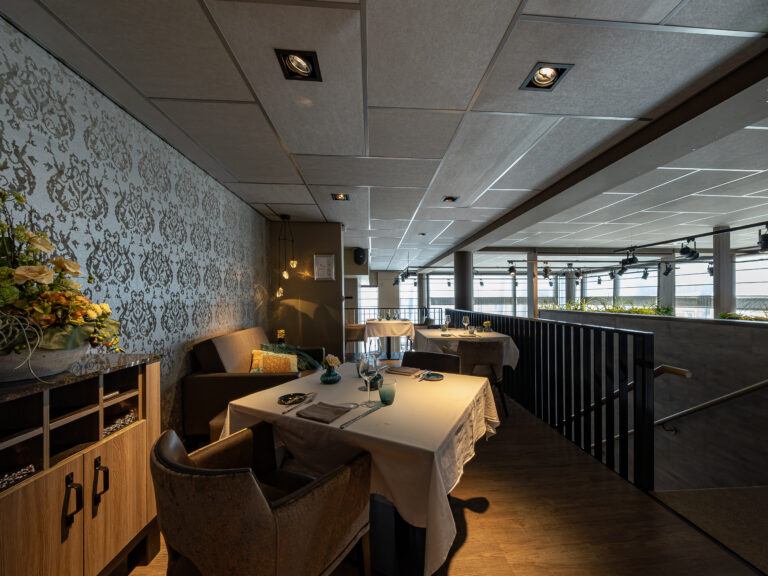 Stijlvol restaurantinterieur met gedekte tafels, sierlijk behang en een trap naar een lager niveau.
