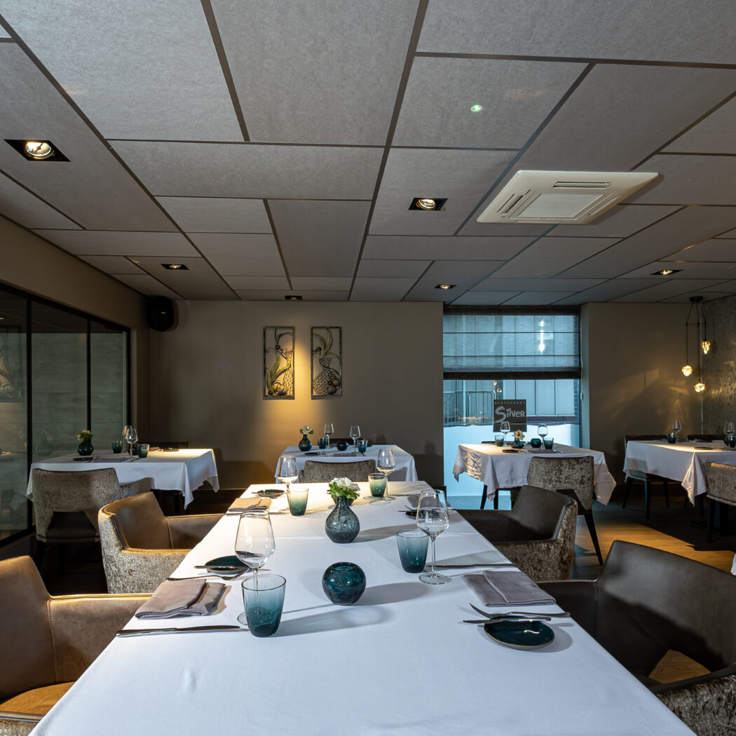 Elegant restaurantinterieur met gedekte tafels, comfortabele stoelen, patroonbehang en sfeervolle verlichting.