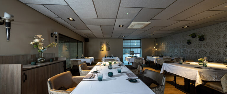 Elegant restaurantinterieur met gedekte tafels, comfortabele stoelen, patroonbehang en sfeervolle verlichting.
