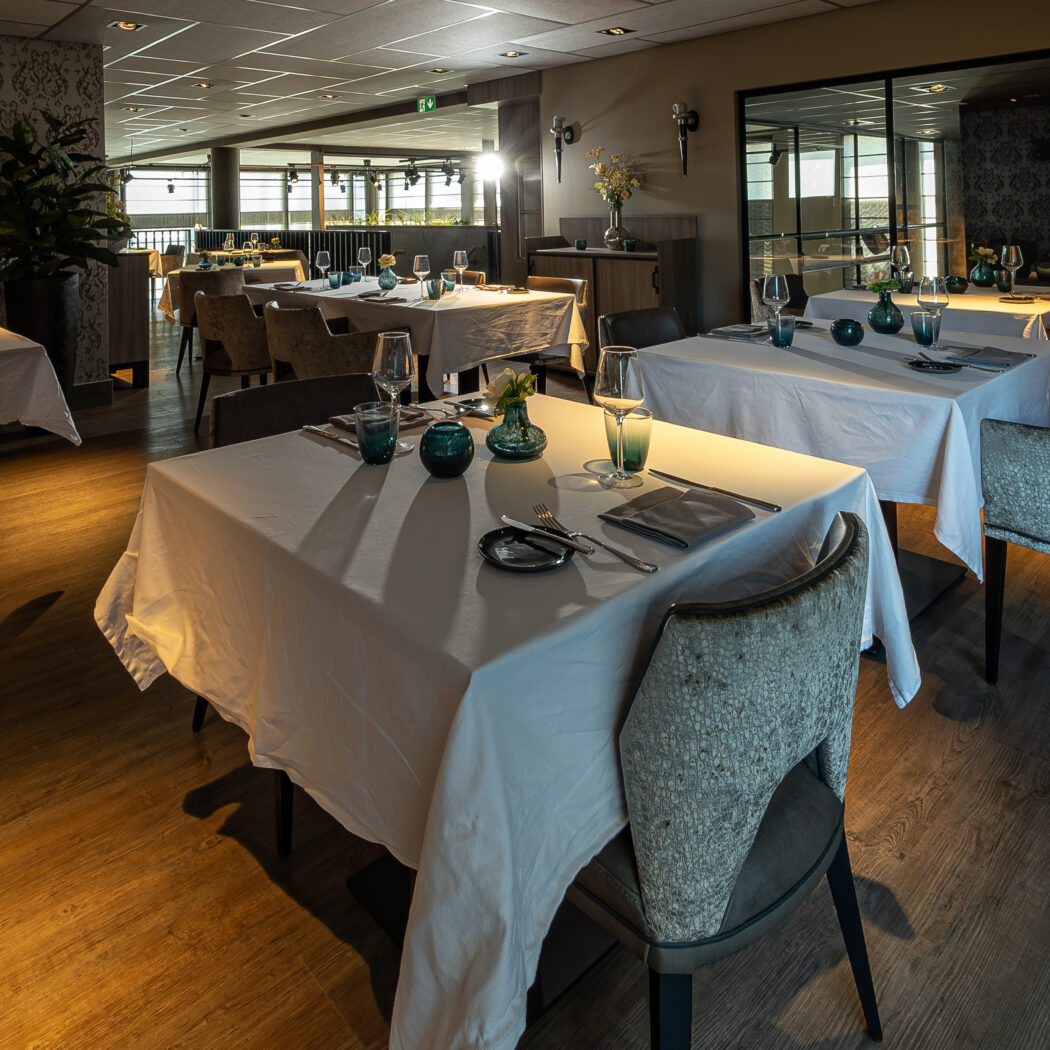 Sfeervol restaurantinterieur met wit gedekte tafels, chique stoelen en wanden met een elegant patroon.