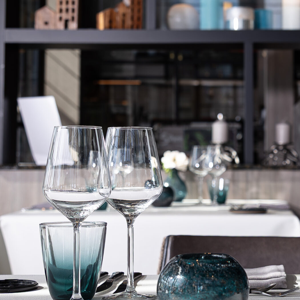 Gedekte tafel in een restaurant met heldere wijnglazen, een groenblauw drinkglas en een decoratieve bol.