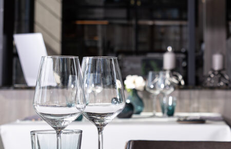Gedekte tafel in een restaurant met heldere wijnglazen, een groenblauw drinkglas en een decoratieve bol.