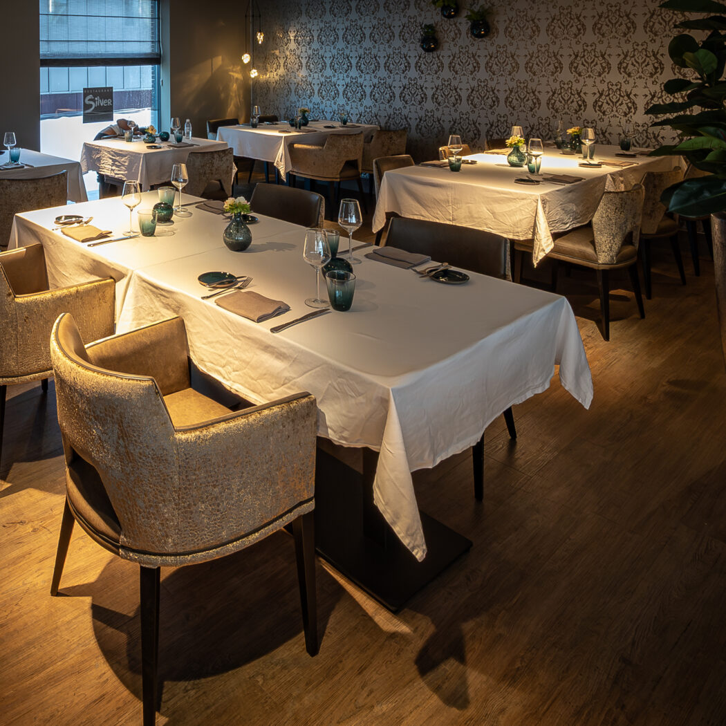 Elegant restaurantinterieur met wit gedekte tafels, sfeervolle verlichting en comfortabele goudkleurige stoelen.