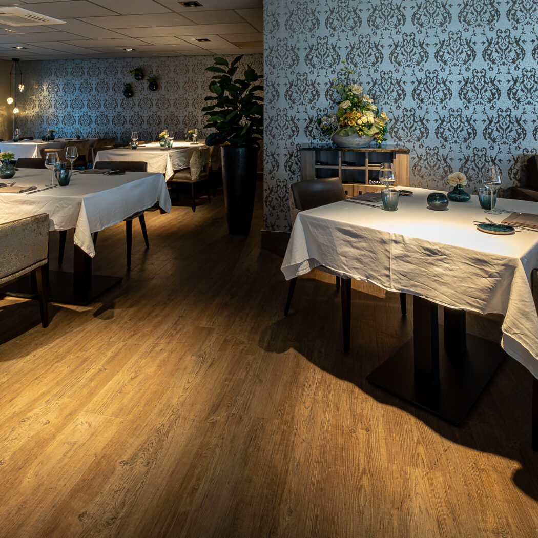 Sfeervol restaurant met gedekte tafels, patroonbehang, houten vloer en een zitgedeelte, inclusief Silven op het raam.