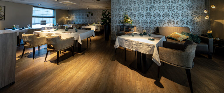 Sfeervol restaurant met gedekte tafels, patroonbehang, houten vloer en een zitgedeelte, inclusief Silven op het raam.