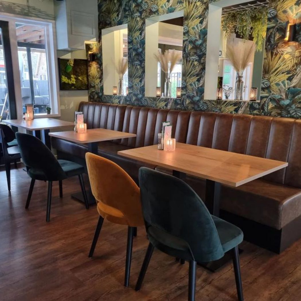 Sfeervol restaurantinterieur met bruine bank, houten tafels met kaarsen, en fluwelen stoelen voor tropisch behang.