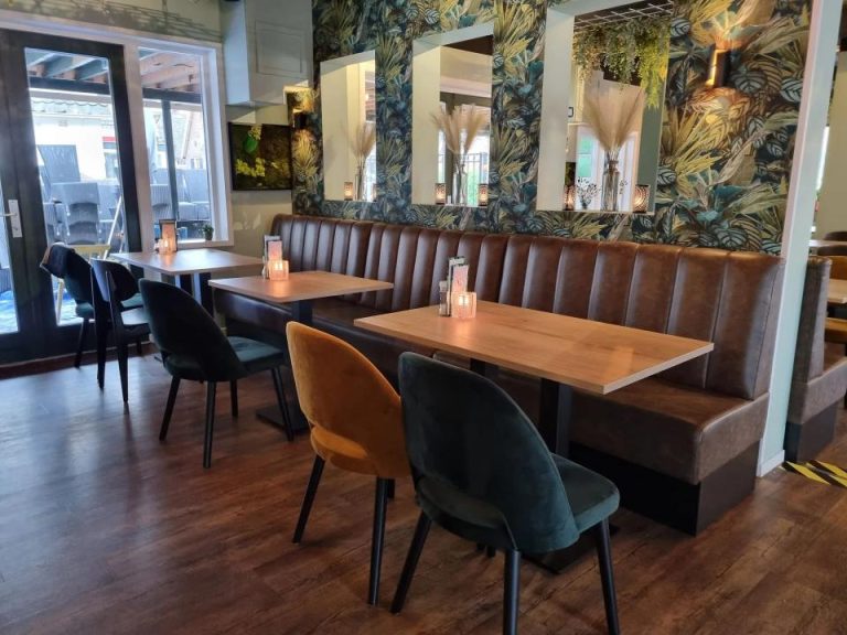 Sfeervol restaurantinterieur met bruine bank, houten tafels met kaarsen, en fluwelen stoelen voor tropisch behang.