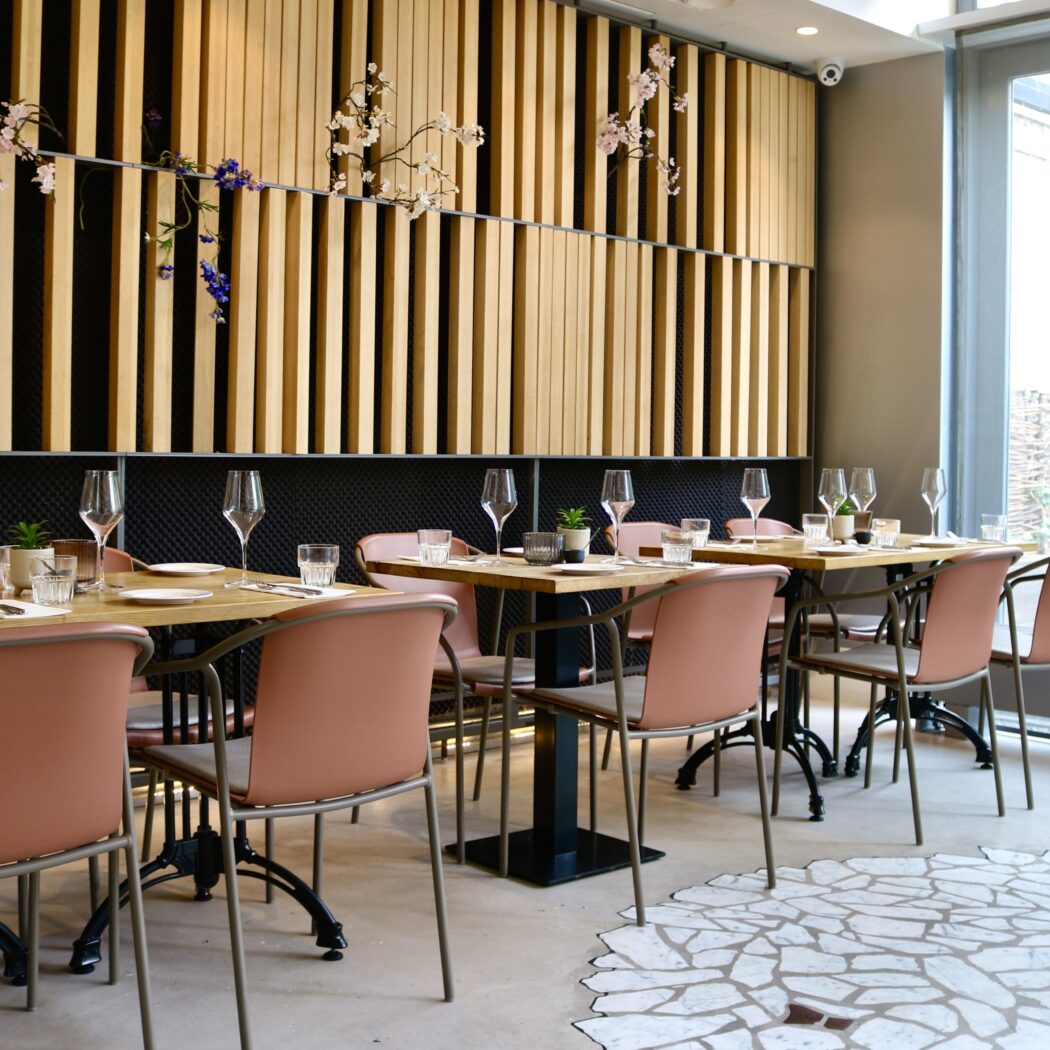 Modern restaurantinterieur met gedekte houten tafels, oudroze stoelen en een decoratieve lattenwand met bloesem.