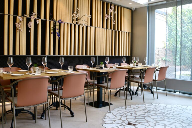 Modern restaurantinterieur met gedekte houten tafels, oudroze stoelen en een decoratieve lattenwand met bloesem.