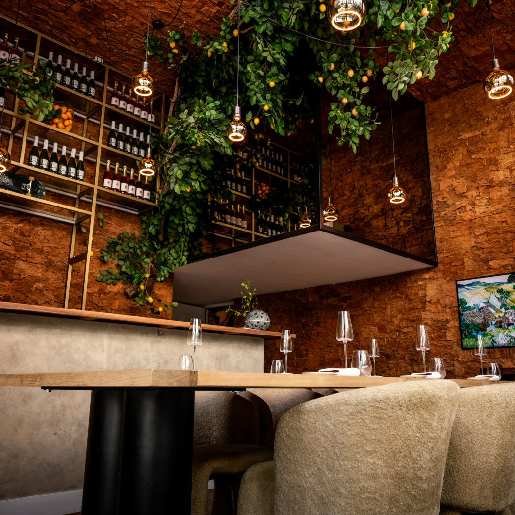 Sfeervol restaurant interieur met bakstenen muren, hangende citroenplanten, wijnen op een plank en een gedekte houten tafel.