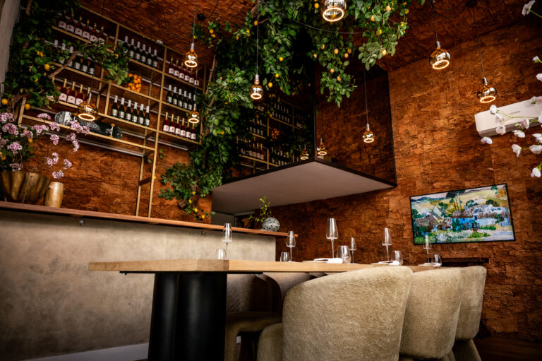 Sfeervol restaurant interieur met bakstenen muren, hangende citroenplanten, wijnen op een plank en een gedekte houten tafel.