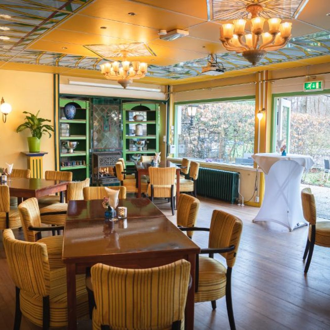 Sfeervolle eetzaal met gele muren, gedessineerd plafond, houten tafels en gestreepte gele stoelen.