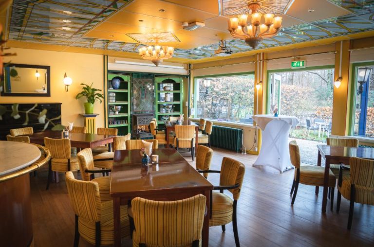 Sfeervolle eetzaal met gele muren, gedessineerd plafond, houten tafels en gestreepte gele stoelen.