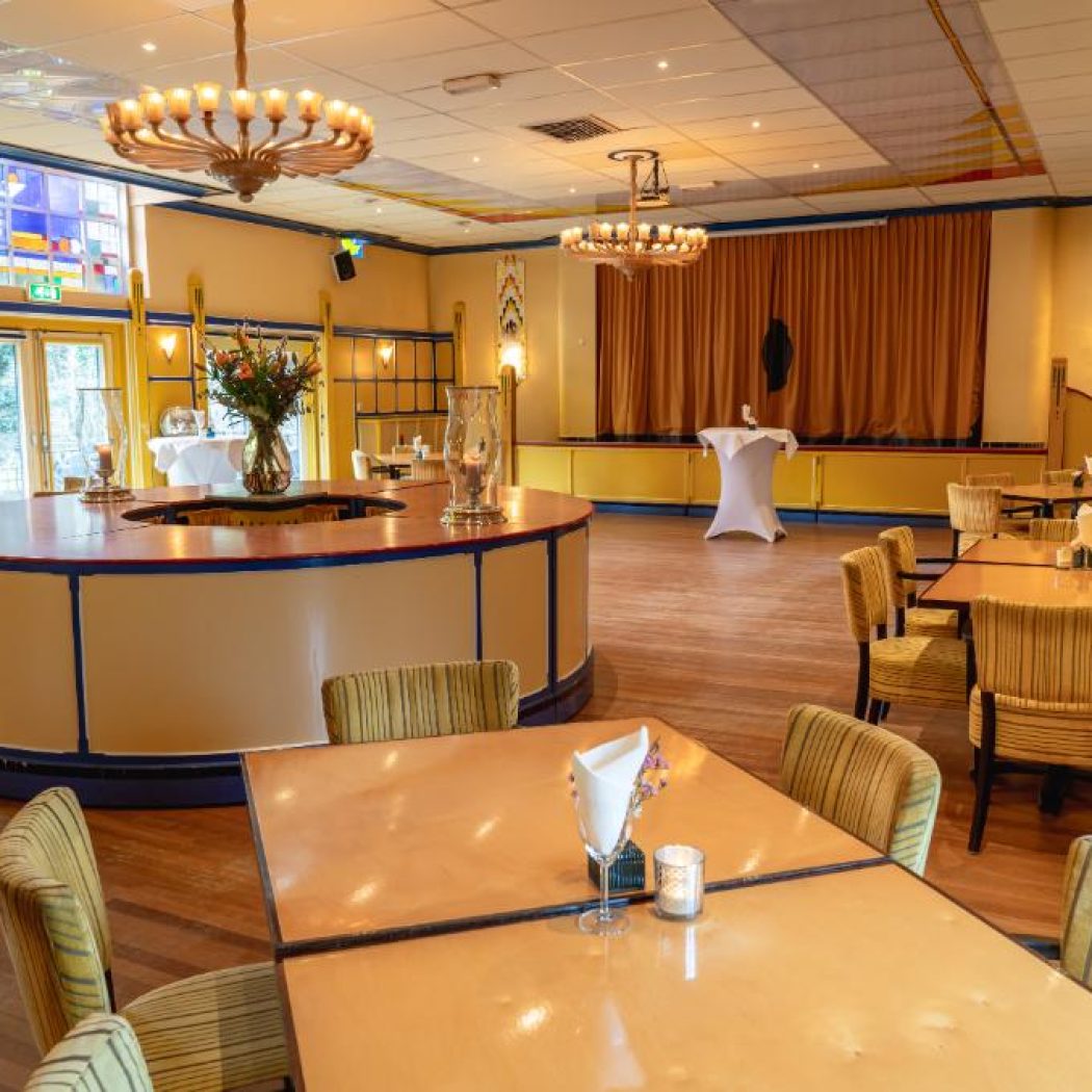 Royale evenementenzaal met houten vloer, ronde bar, goudgele stoelen en gebrandschilderd glas, sfeervol verlicht.