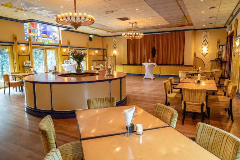 Royale evenementenzaal met houten vloer, ronde bar, goudgele stoelen en gebrandschilderd glas, sfeervol verlicht.