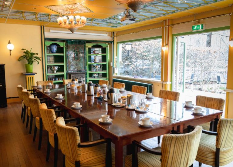 Sfeervolle vergaderzaal met decoratief plafond, lange houten tafel met koffieservies, groene kasten en winterzicht.