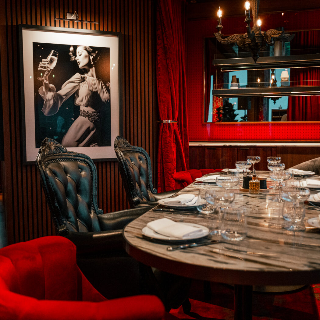 Luxe restaurant met gedekte marmeren tafel, donkere leren stoelen, rode fluwelen accenten en een kunstwerk van een vrouw.