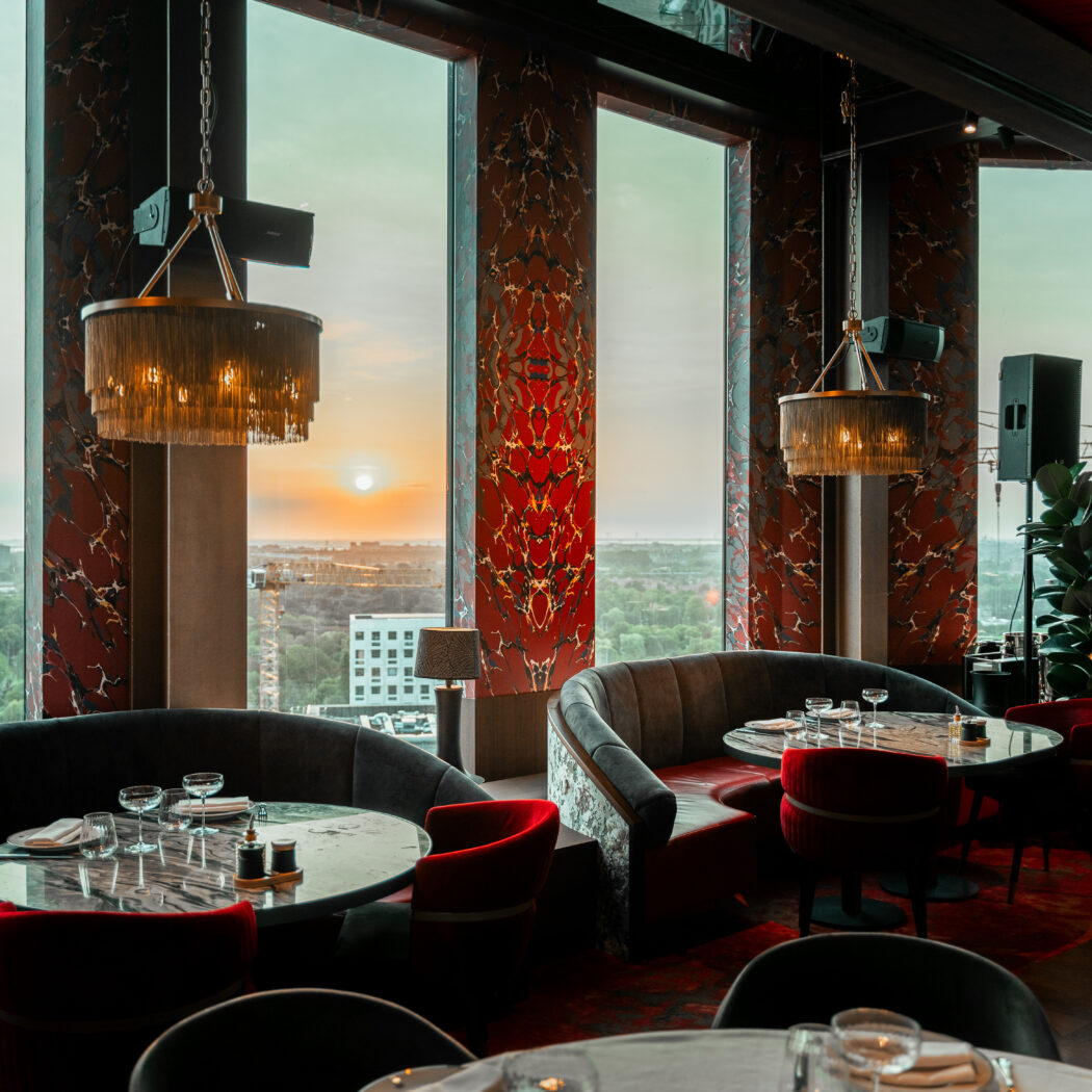 Luxe restaurant met rood marmeren pilaren, gouden kroonluchters en donkere banken bij zonsondergang.