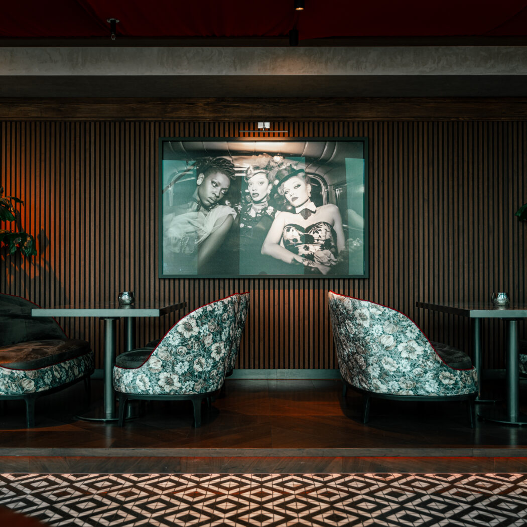 Sfeervolle lounge met floral design stoelen, houten wandpanelen en groot zwart-wit portret.