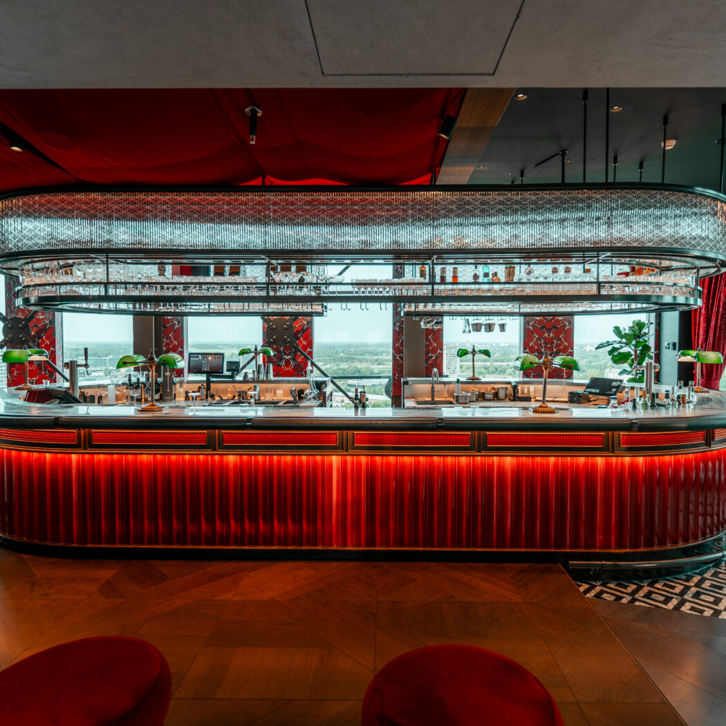 Luxe rooftop bar Ventuno met rood verlichte balie, glazenrek en panoramisch uitzicht.