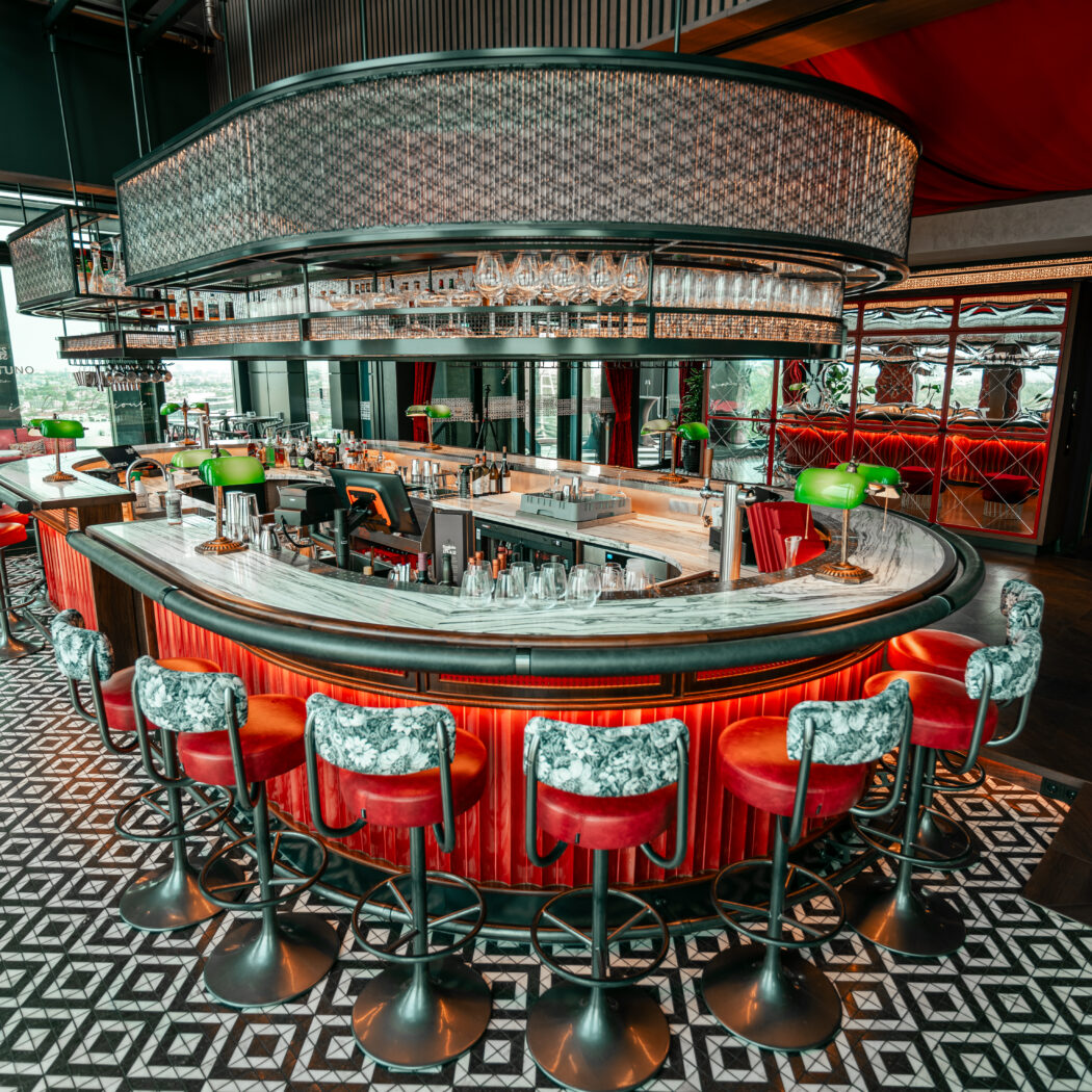 Luxe ronde bar in Ventuno Lounge met rode krukken, marmeren blad en geometrische vloertegels.