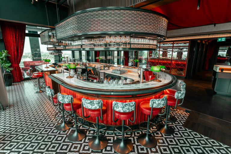 Luxe ronde bar in Ventuno Lounge met rode krukken, marmeren blad en geometrische vloertegels.