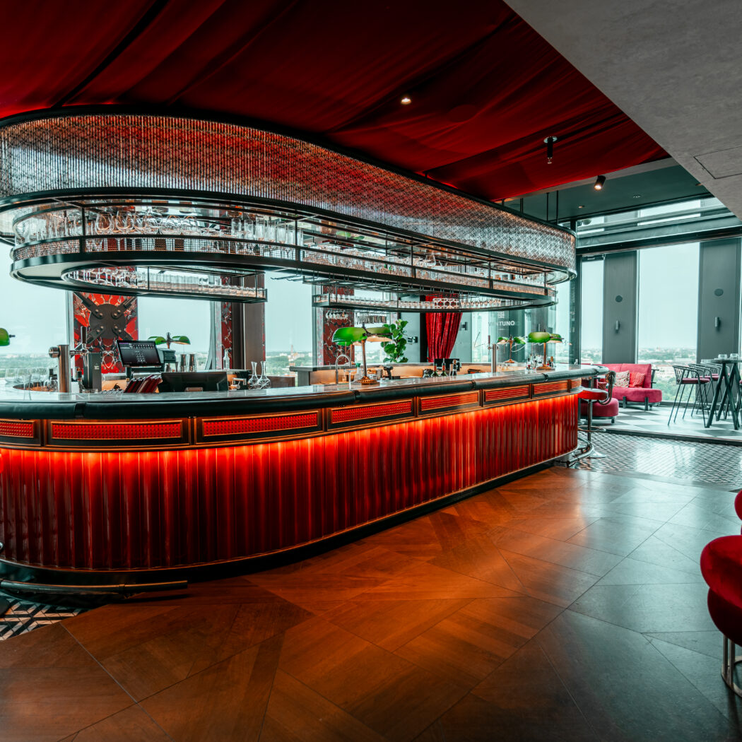 Stijlvolle bar met golvende rode verlichting, groene tafellampen en een panoramisch uitzicht over de stad.