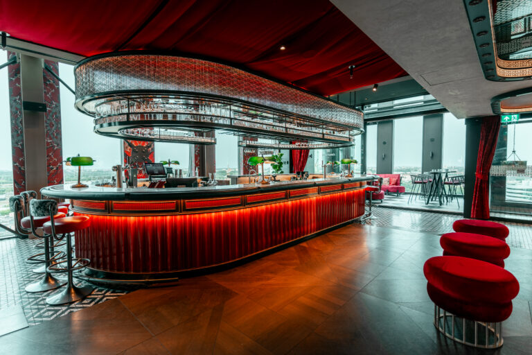 Stijlvolle bar met golvende rode verlichting, groene tafellampen en een panoramisch uitzicht over de stad.