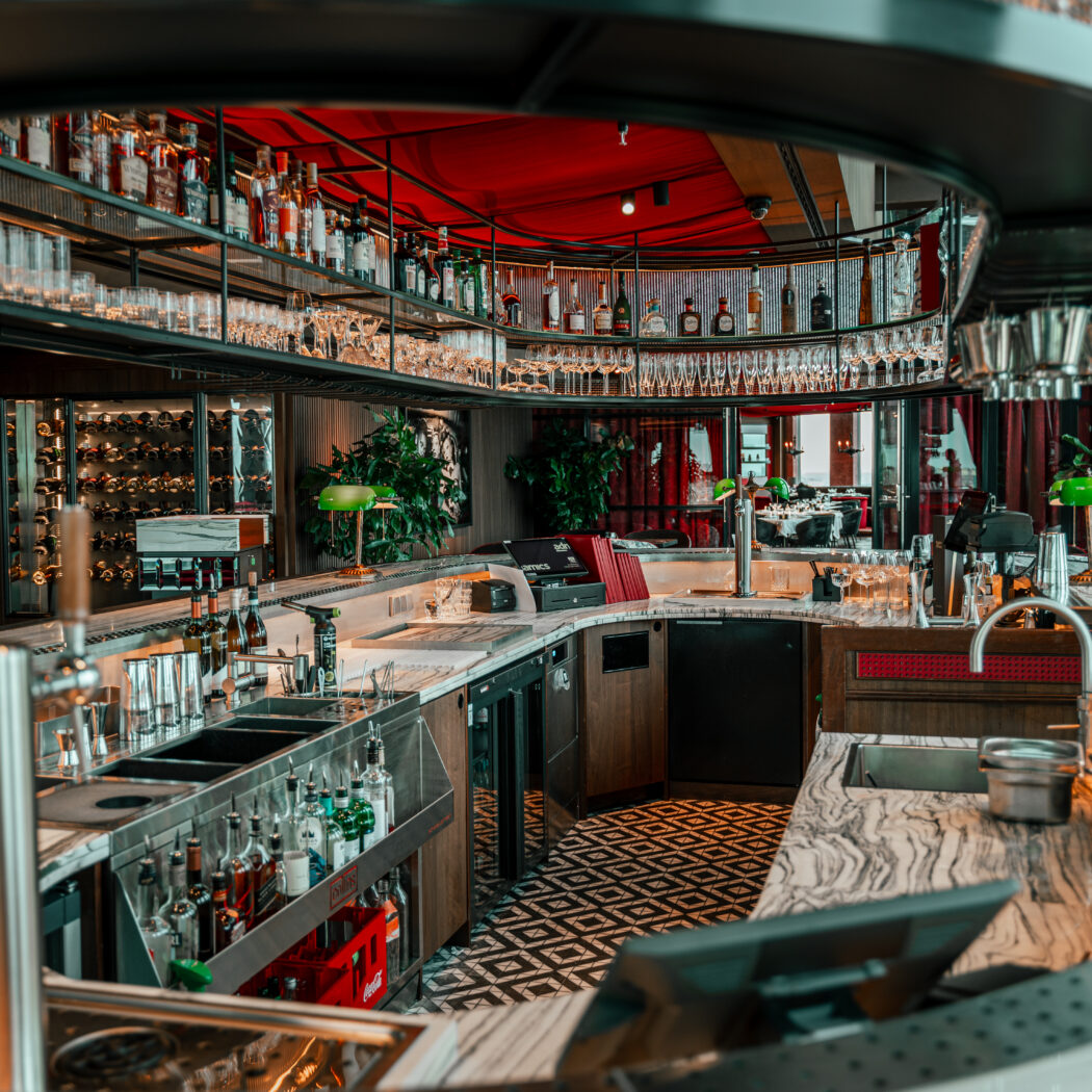 Luxe barinterieur met marmeren balie, gevulde schappen, groene bureaulampen en een rood accentplafond.