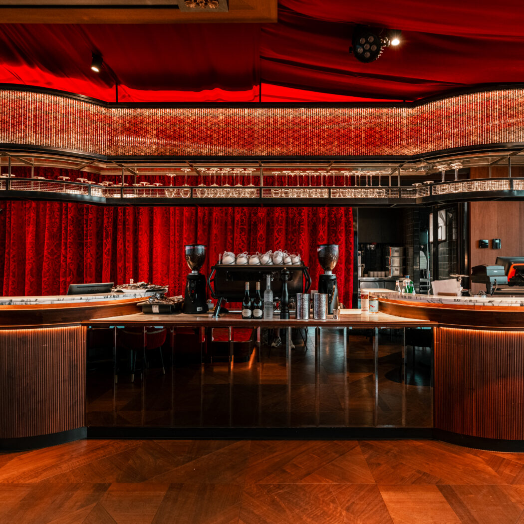 Luxe moderne bar met donkerhout, marmeren blad, rode gordijnen en een sierlijke, verlichte glasplank.