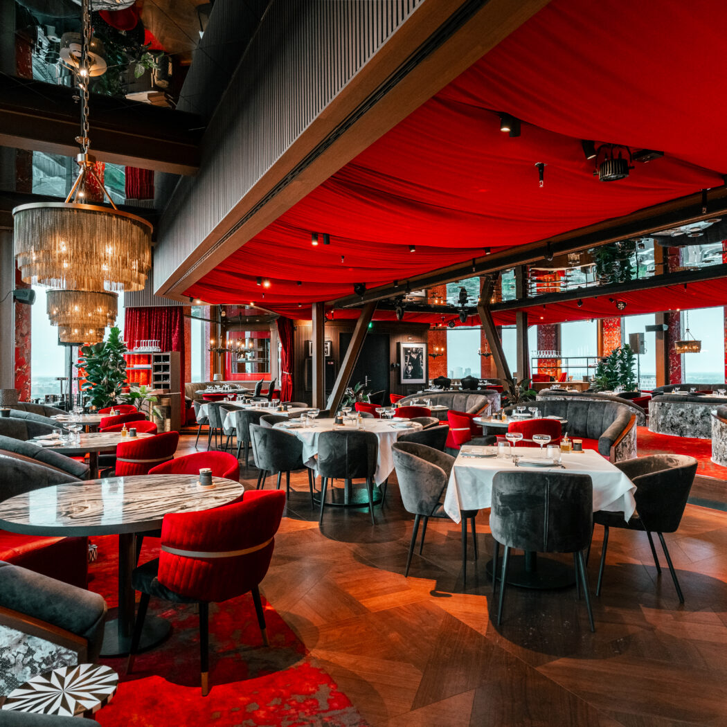 Stijlvol restaurant met rode draperieën, donkerhouten vloer, fluwelen zitmeubels en een weids uitzicht.