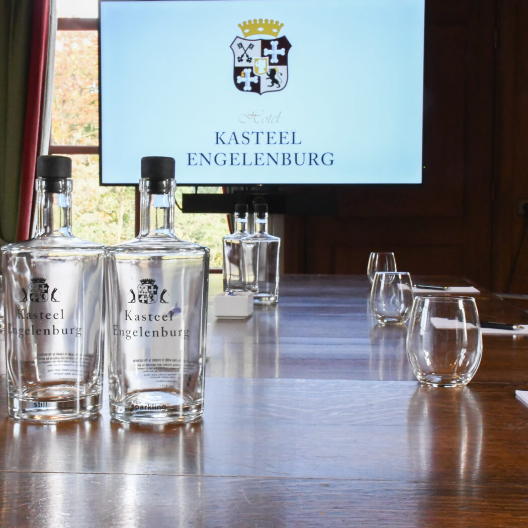 Kasteel Engelenburg waterflessen en glazen op houten vergadertafel met scherm Hotel Kasteel Engelenburg.