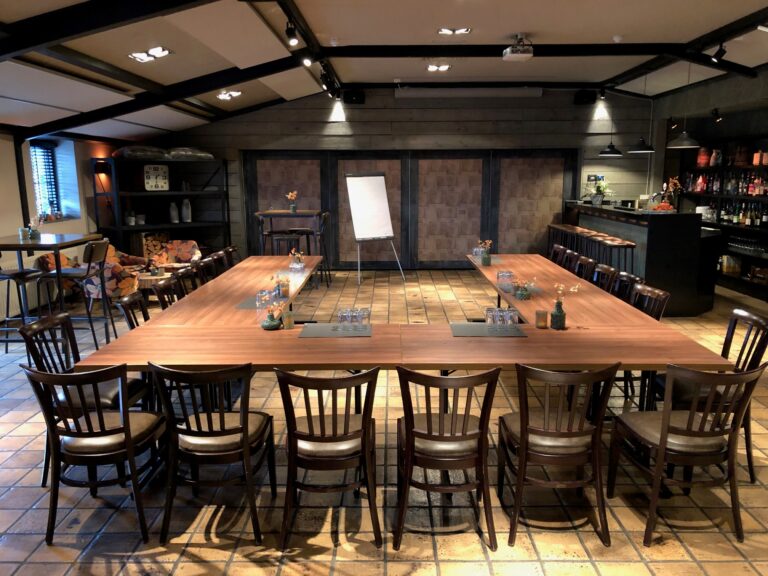 Ruime conferentiezaal met U-vormige houten tafel, voorbereid voor een vergadering, inclusief bar en zithoek.